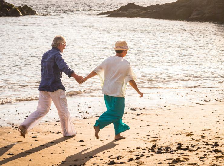 Coppia di anziani che si tiene per mano durante una passeggiata sulla spiaggia