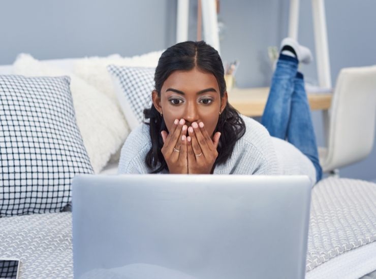 Ragazza sul letto con le mani davanti alla bocca e PC 